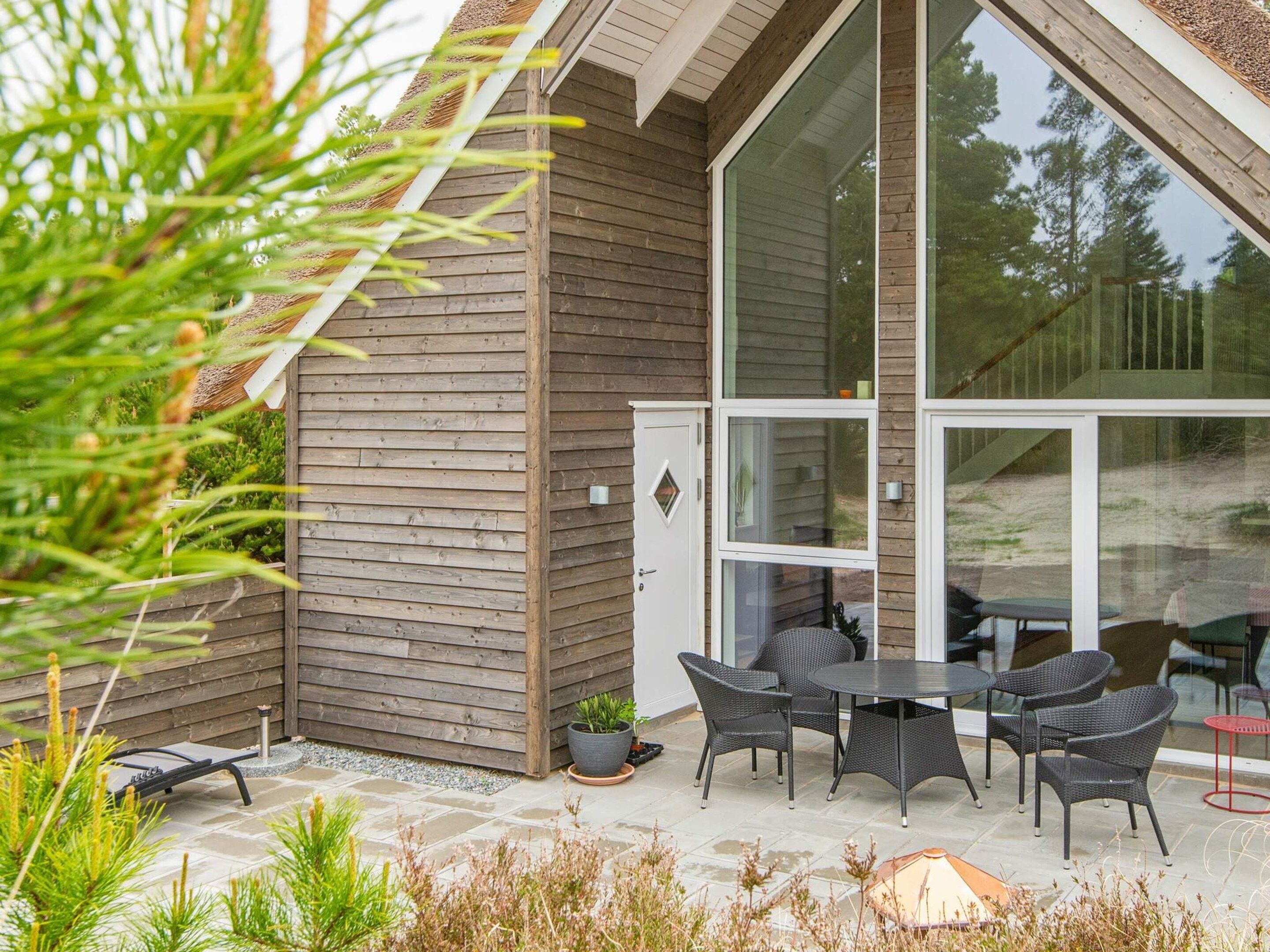 Une maison moderne dotée d’un patio comprenant une table et des chaises, une plante en pot et une porte.