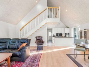 A modern living space with a leather sofa, a patterned rug, a dining table, and a kitchen area with white cabinets.