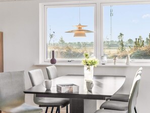 Un comedor moderno con una gran mesa y sillas, una lámpara colgante y vistas a un paisaje rural a través de amplios ventanales.