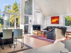 Una sala de estar moderna con chimenea, asientos cómodos y grandes ventanales con vistas a árboles.