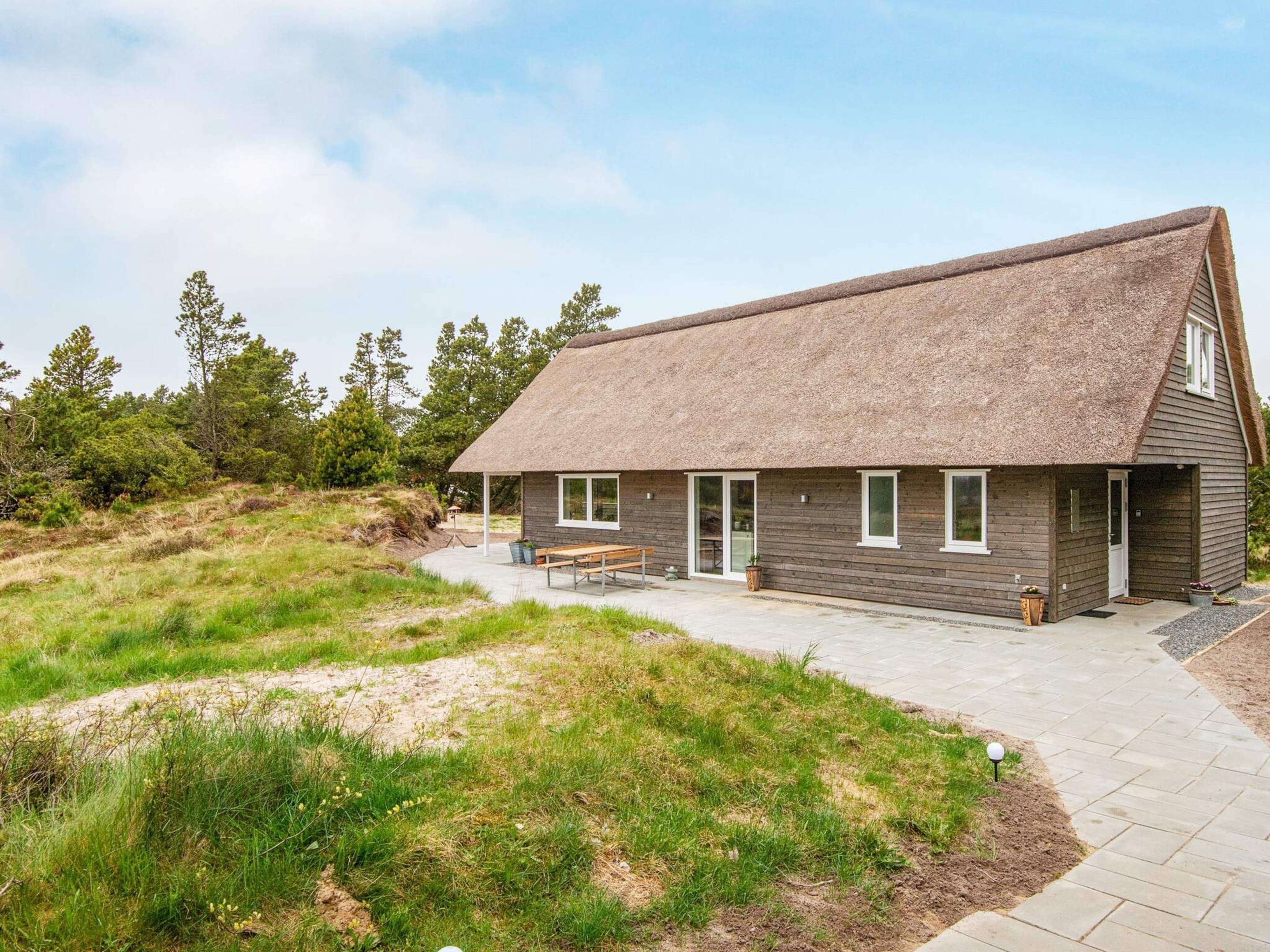 Een landelijke constructie met rieten dak, houten wanden en een geplaveid entreegebied met een bank.