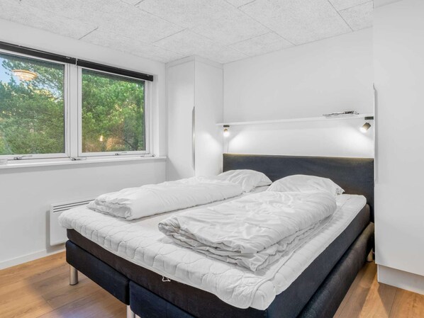 A modern bedroom with a bed, a window, and a wall-mounted light fixture.