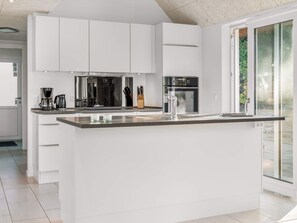 Una cocina moderna con armarios blancos, una isla central y un amplio ventanal.