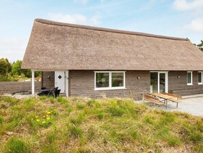 A modern building with a thatched roof, wooden walls, and a bench outside.