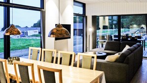 A modern interior with a dining area, sofa, and large windows offering views of the outdoors. - 8 Person Holiday Home in Sjolund-by Traum (Sjølund)