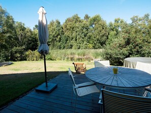 Una terraza exterior con una mesa redonda y sillas, una sombrilla y un banco de madera.