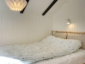 A bed with a white sheet and a patterned blanket, a wooden headboard, and a pendant light fixture.