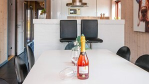 Un coin repas moderne avec une table blanche, deux chaises noires, une bouteille de vin et un verre.
