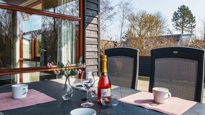 Un espace de restauration en plein air avec une table dressée pour deux personnes, agrémenté d’une bouteille de champagne, de deux tasses blanches et d’un verre.