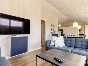 A modern living room with a flat-screen TV, a sofa, a coffee table, and a kitchen area in the background.