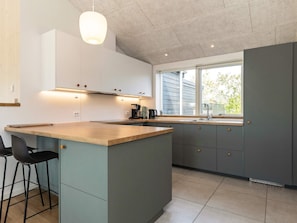 A modern kitchen with a central island, bar stools, a window with a view, and built-in cabinets.
