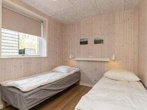 A room with two single beds, a window, and a wall-mounted shelf with two pictures.