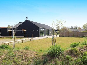 A black building with a sloped roof, a fenced yard, and a small tree. - 5 Star Holiday Home in Hadsund (Hadsund)