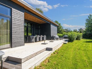 Et moderne hus med en overdækket terrasse, havemøbler og en velplejet græsplæne.