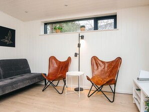 A modern living room with a grey sofa, two leather chairs, a small white table, and a floor lamp. - 5 Star Holiday Home in Ebeltoft (Ebeltoft)
