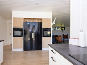 A modern kitchen with a double-door refrigerator, built-in oven, and a wooden cabinet. - 5 Star Holiday Home in Ebeltoft (Ebeltoft)