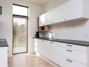 A modern kitchen with white cabinets, a black countertop, and a window with a view of greenery. - 5 Star Holiday Home in Ebeltoft (Ebeltoft)
