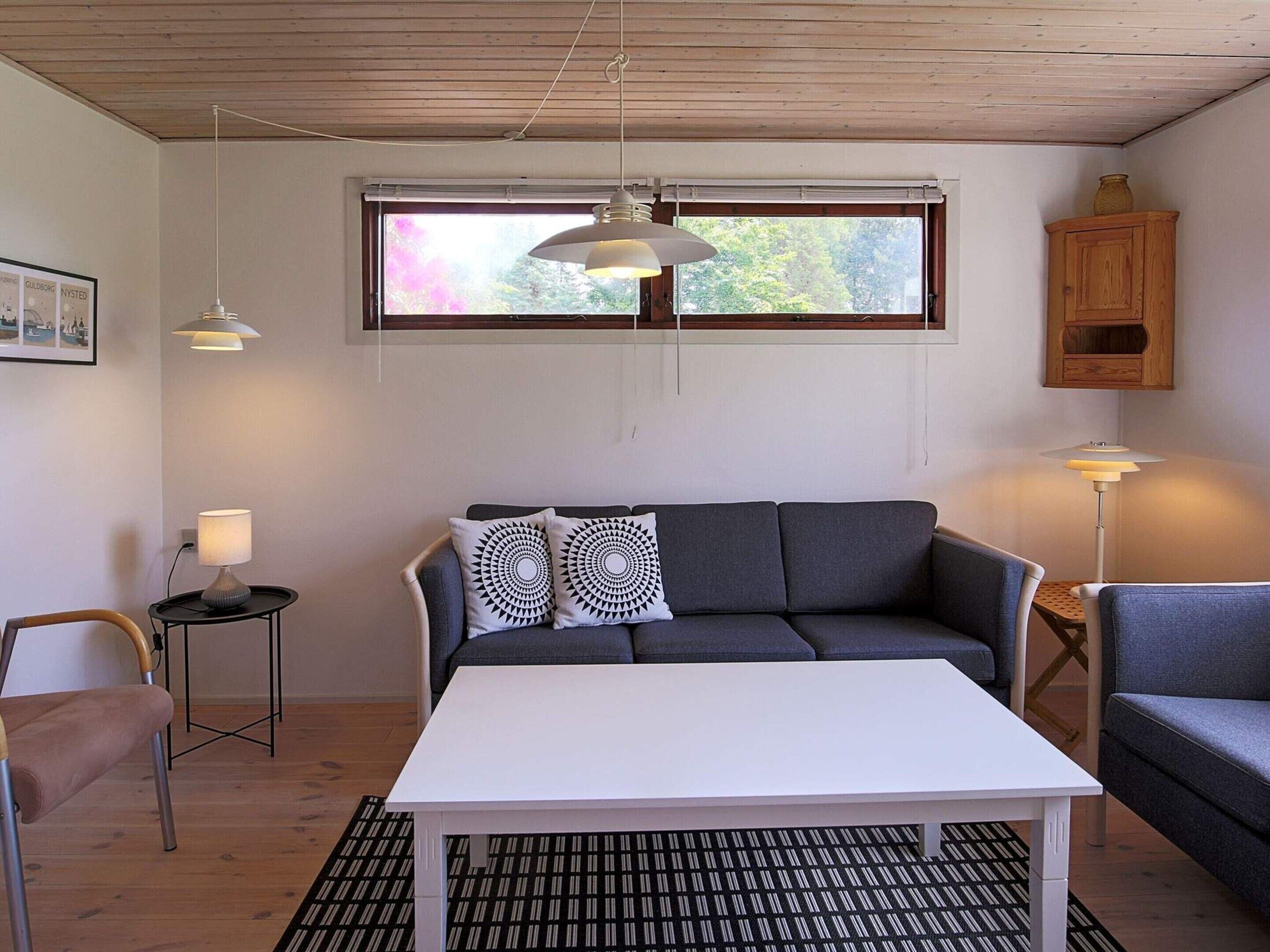 Een moderne woonkamer met een grijze bank, een witte salontafel en een kamerbreed tapijt met dessin.