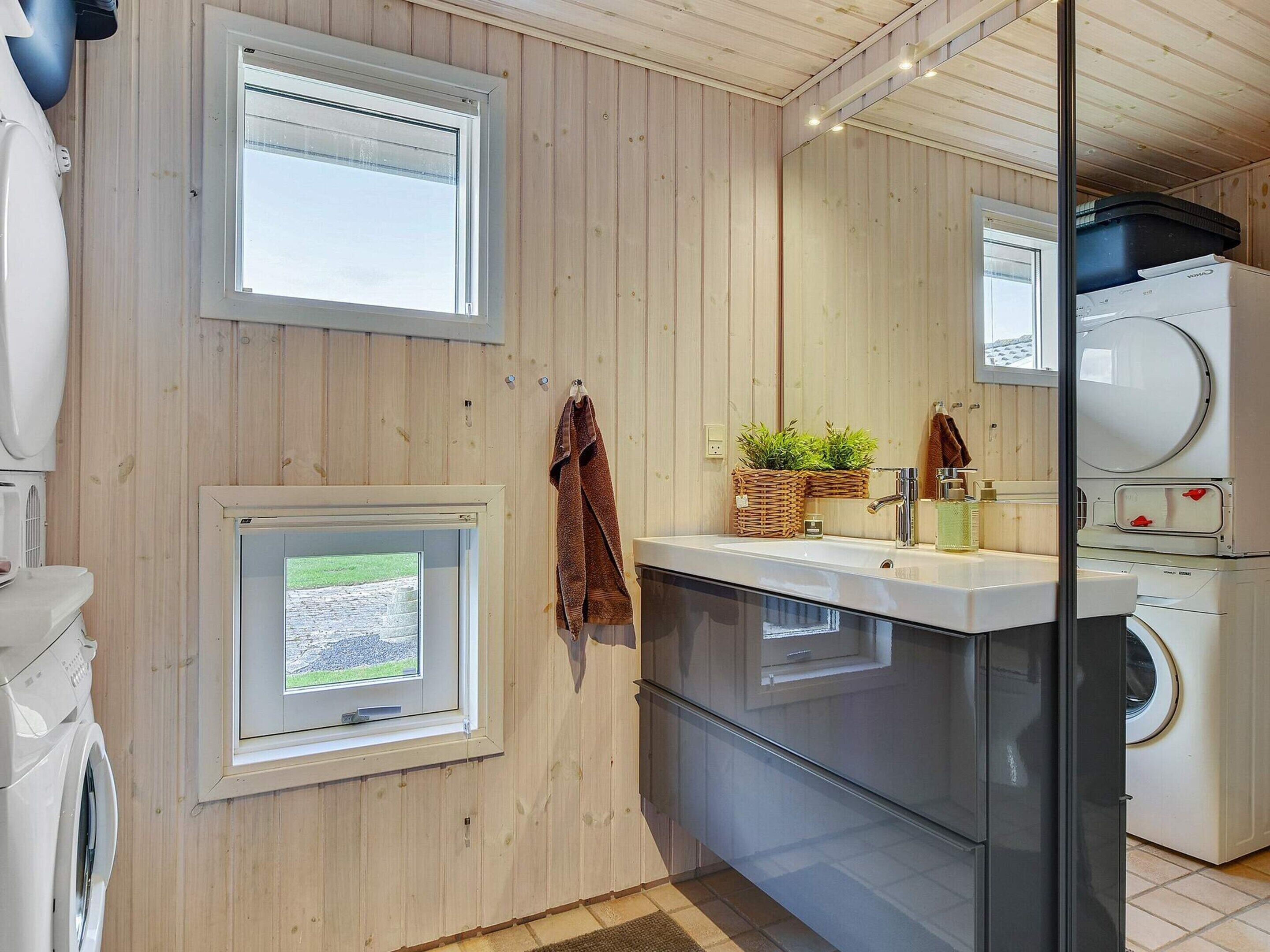 Un baño moderno con paredes de madera, un espejo grande, un lavamanos con grifo y una lavadora.