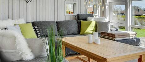 A modern living room with a wooden table, grey sofa, and a potted plant.