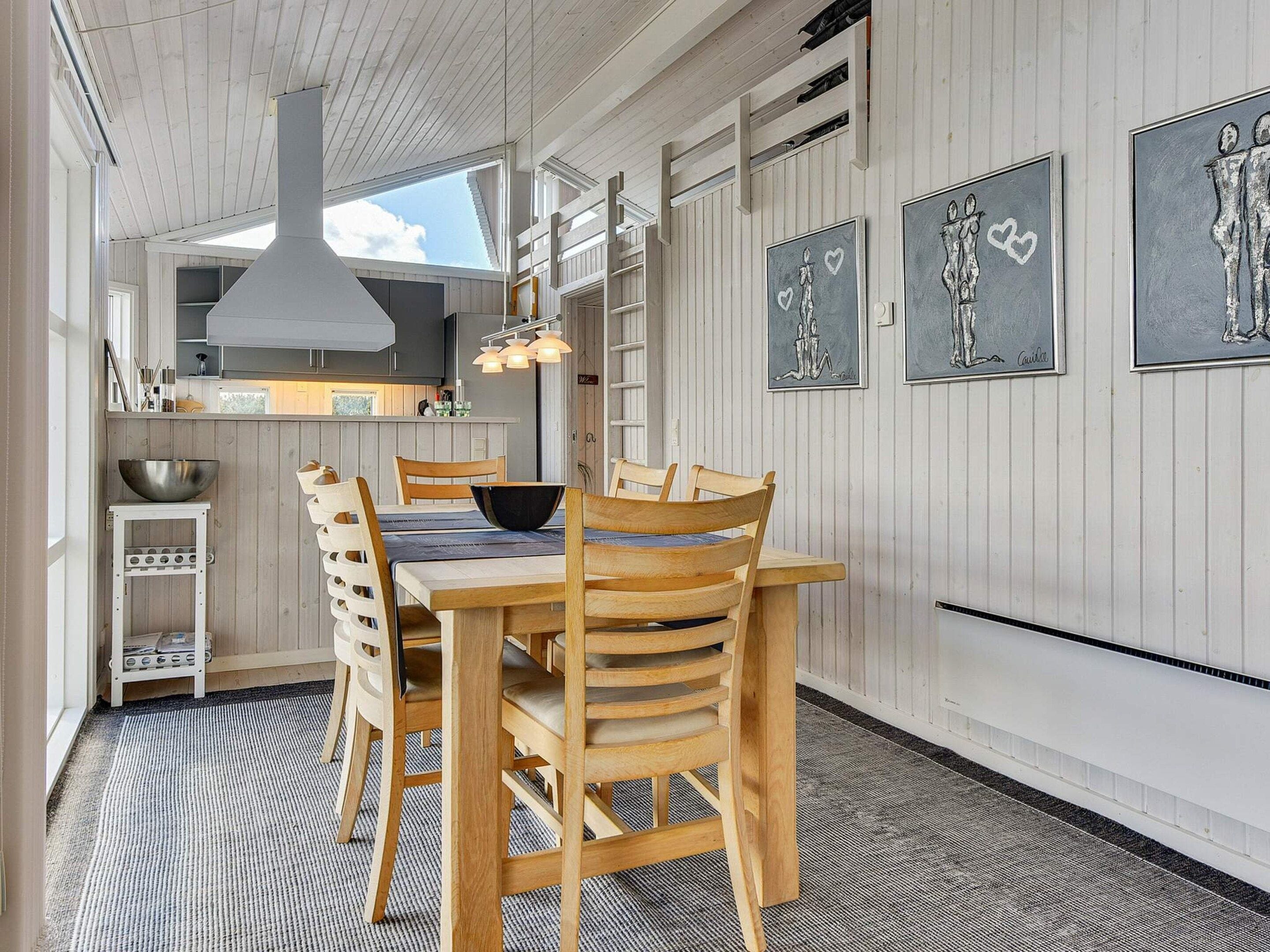 A dining area with a wooden table and chairs, a hanging light fixture, and artwork on the walls.