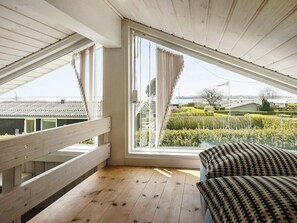 Quarto com teto inclinado, amplas janelas e vista para um jardim ajardinado.