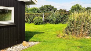 Ein schwarzes Gebäude mit einem Fenster, einem Rasen und einer Hecke im Hintergrund.