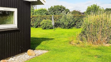 A black building with a window, a grassy yard, and a hedge.