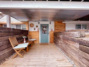 A covered wooden deck with a table and chairs, a door, and a stone wall.