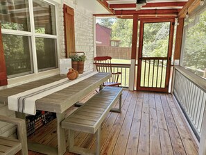 A wooden deck with a bench and table, a door leading outside, and a view of a house in the background.