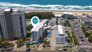 Un complexe hôtelier situé sur la côte, composé de plusieurs bâtiments, doté d’aires de stationnement et offrant une vue sur la plage.
