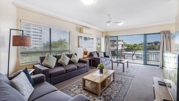 A spacious living room with a grey sofa set, a wooden coffee table, and a large TV.