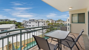 A balcony with a table and chairs, overlooking a pool and buildings.
