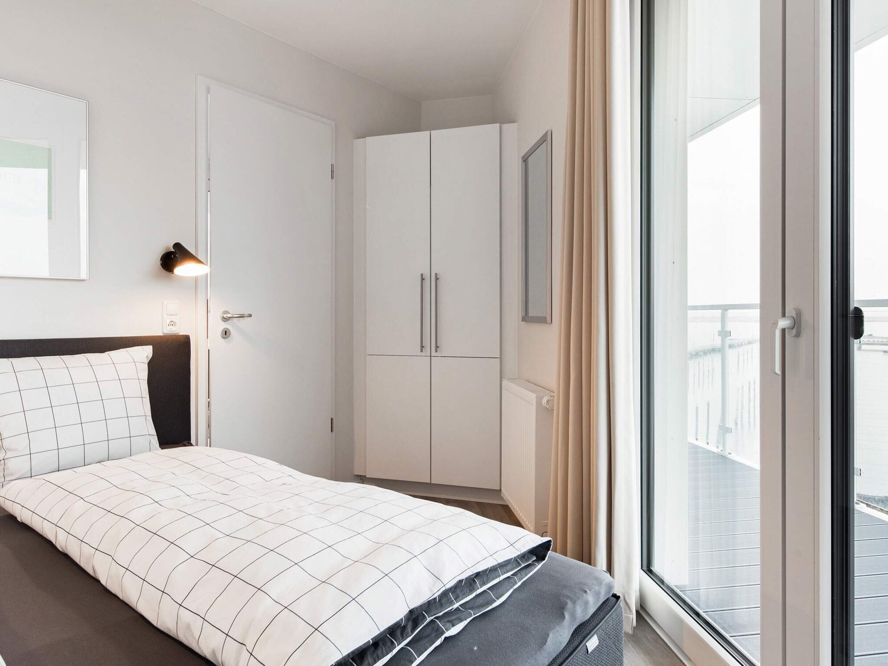 Ein Schlafzimmer mit einem Bett, einem Kleiderschrank, einer Heizung und einem Fenster mit Vorhängen.