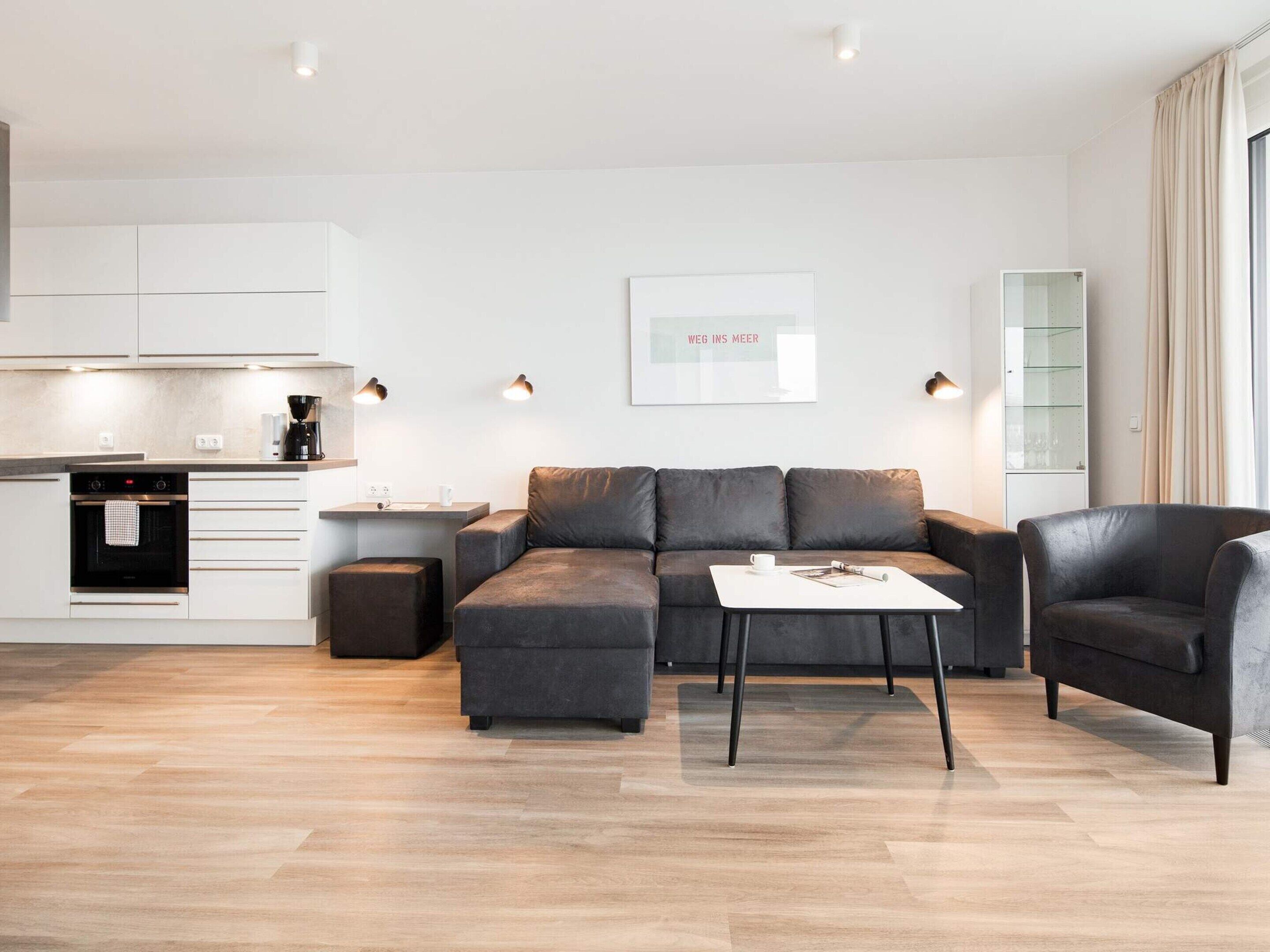 Ein modernes Wohnzimmer mit grauem Sofa, einem Couchtisch und einem Essbereich, mit einer Küche im Hintergrund.