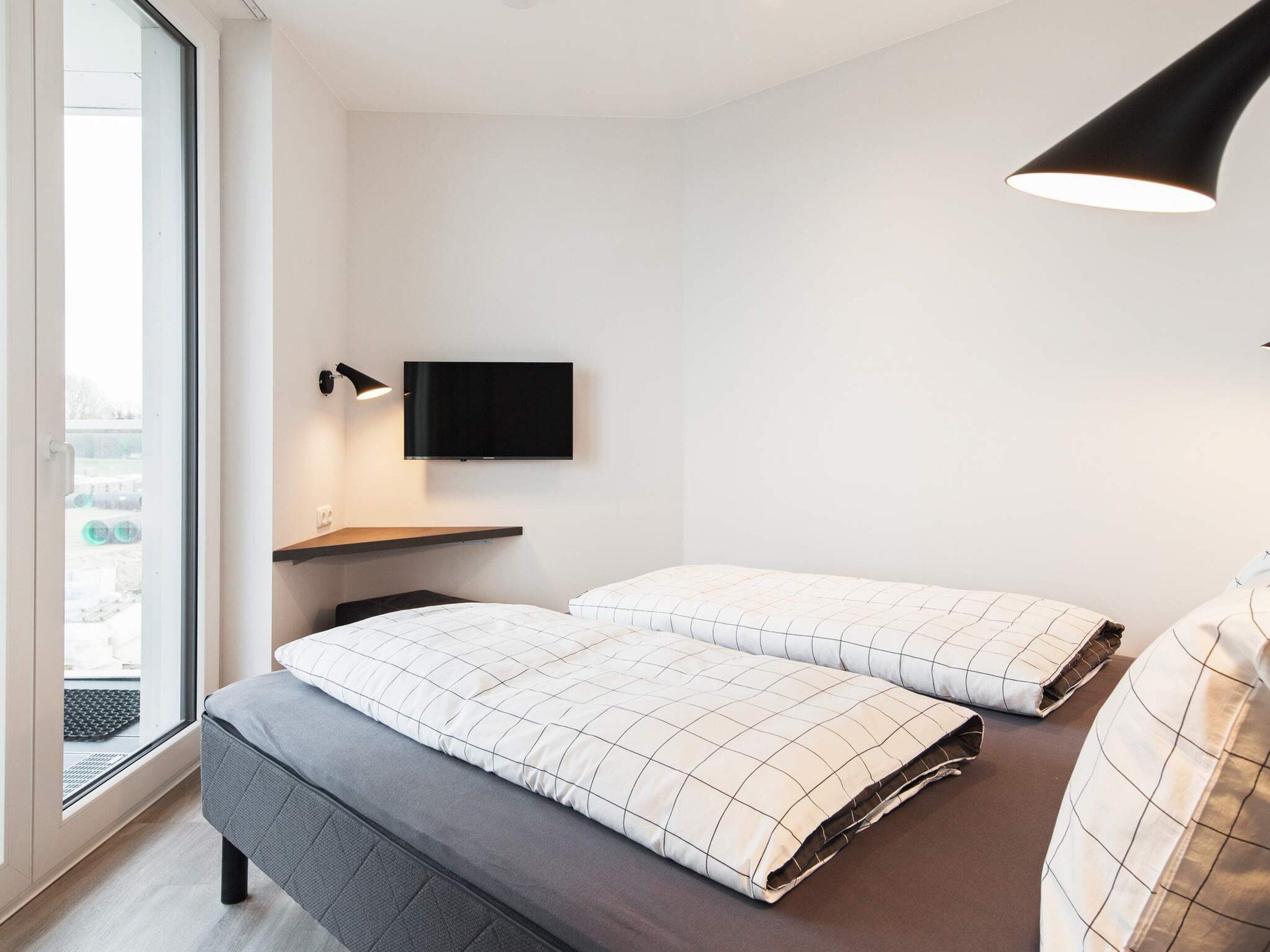 Una camera da letto moderna con un letto, una TV a muro e una finestra.