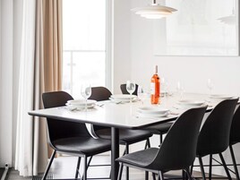 Un comedor con una mesa blanca, sillas negras y una botella de vino.