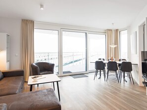 A modern hotel room with a balcony, a dining area, and a seating area with a sofa and armchairs. - 5 Star Holiday Home in Wendtorf (Wendtorf)