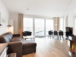 Una sala moderna con sofá, una mesa de comedor con sillas, chimenea y grandes ventanales con vistas a la ciudad.