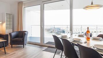 Un comedor moderno con una mesa grande para cuatro personas, vistas de la ciudad a través de amplios ventanales y un balcón con barandilla.