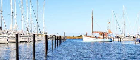 En småbåtshamn med flera segelbåtar förtöjda vid träbryggor.
