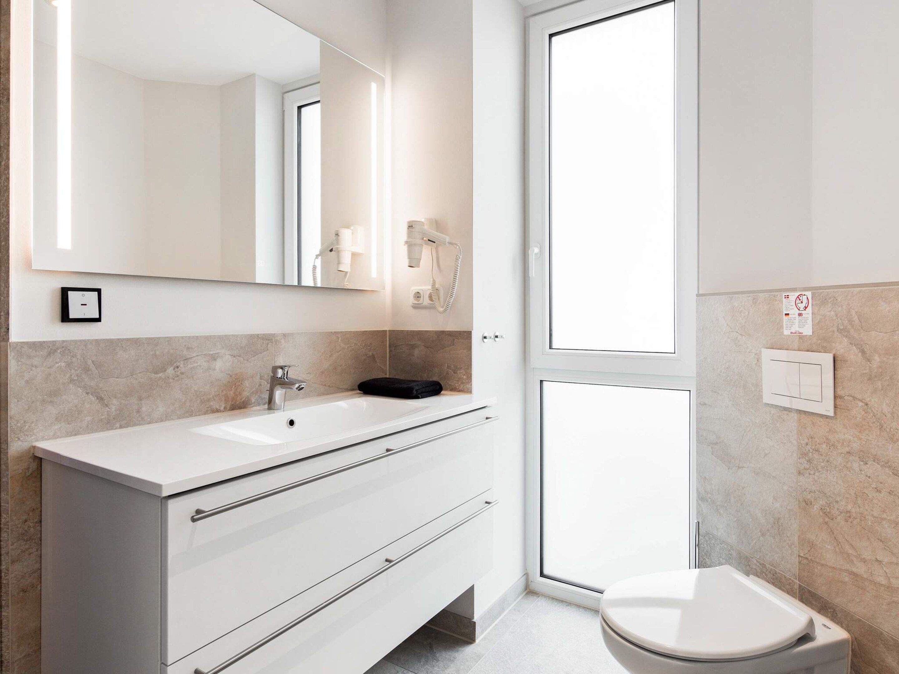 Une salle de bain moderne avec un meuble-lavabo blanc, un miroir, un évier, une serviette et des toilettes.