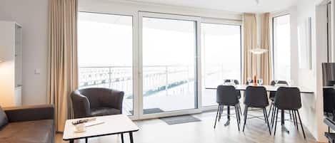 Een moderne hotelkamer met een bank, een eettafel met stoelen, een televisie en grote ramen met uitzicht op de stad.