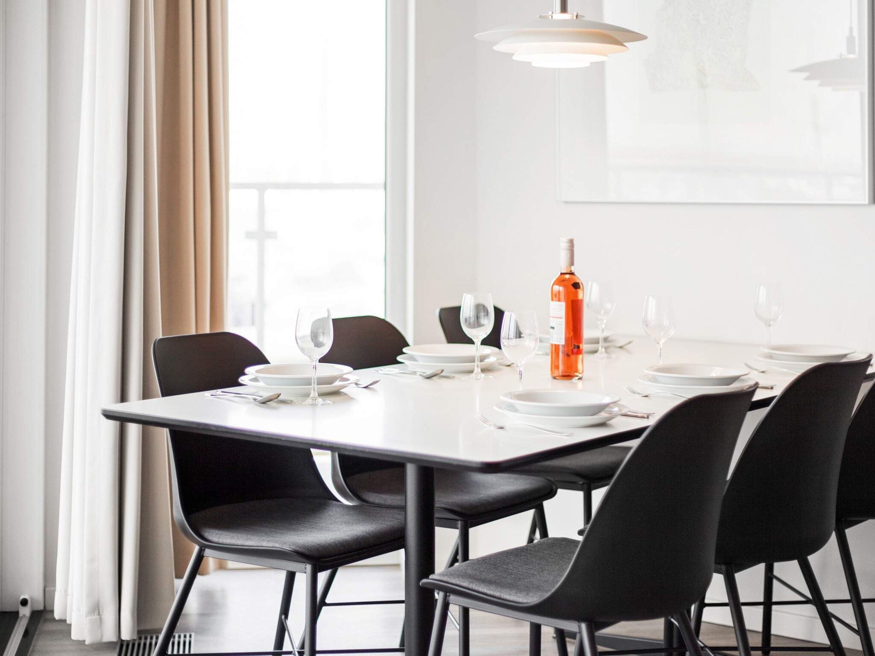 Un coin repas avec une table dressée pour quatre personnes, des chaises, une bouteille de vin et des verres.