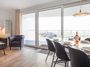 A modern dining area with a table set for two, large windows offering a view of the city, and a hanging light fixture. - 5 Star Holiday Home in Wendtorf (Wendtorf)