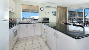 A modern kitchen with white cabinets, a black countertop, a microwave, and a sink. There is a window with a view of buildings and a clock on the wall.