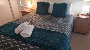 A neatly made bed with a patterned bedspread, two pillows, and a rolled towel on the bed.