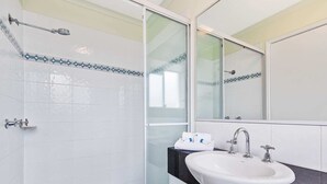 A bathroom with white tiled walls, a glass shower enclosure, a white sink with a black countertop, and a large mirror.