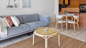 Uma sala de estar moderna com um sofá cinzento, uma mesa de vime e um espaço de refeições com cadeiras de madeira.