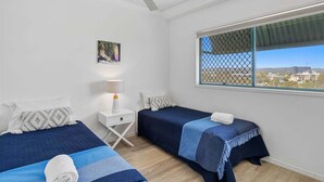 Un dormitorio con dos camas, un ventilador de techo, una ventana con vistas y una mesita de noche con una lámpara.